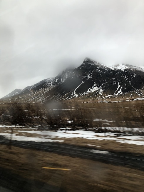 The deep brown volcanic mountains of Iceland crescendo in a spiky peak, snow spotting the shoulders and filling in the ridges all the way down the deep brown form. Viewed while traveling in the car, the foreground blurs as we drive by.