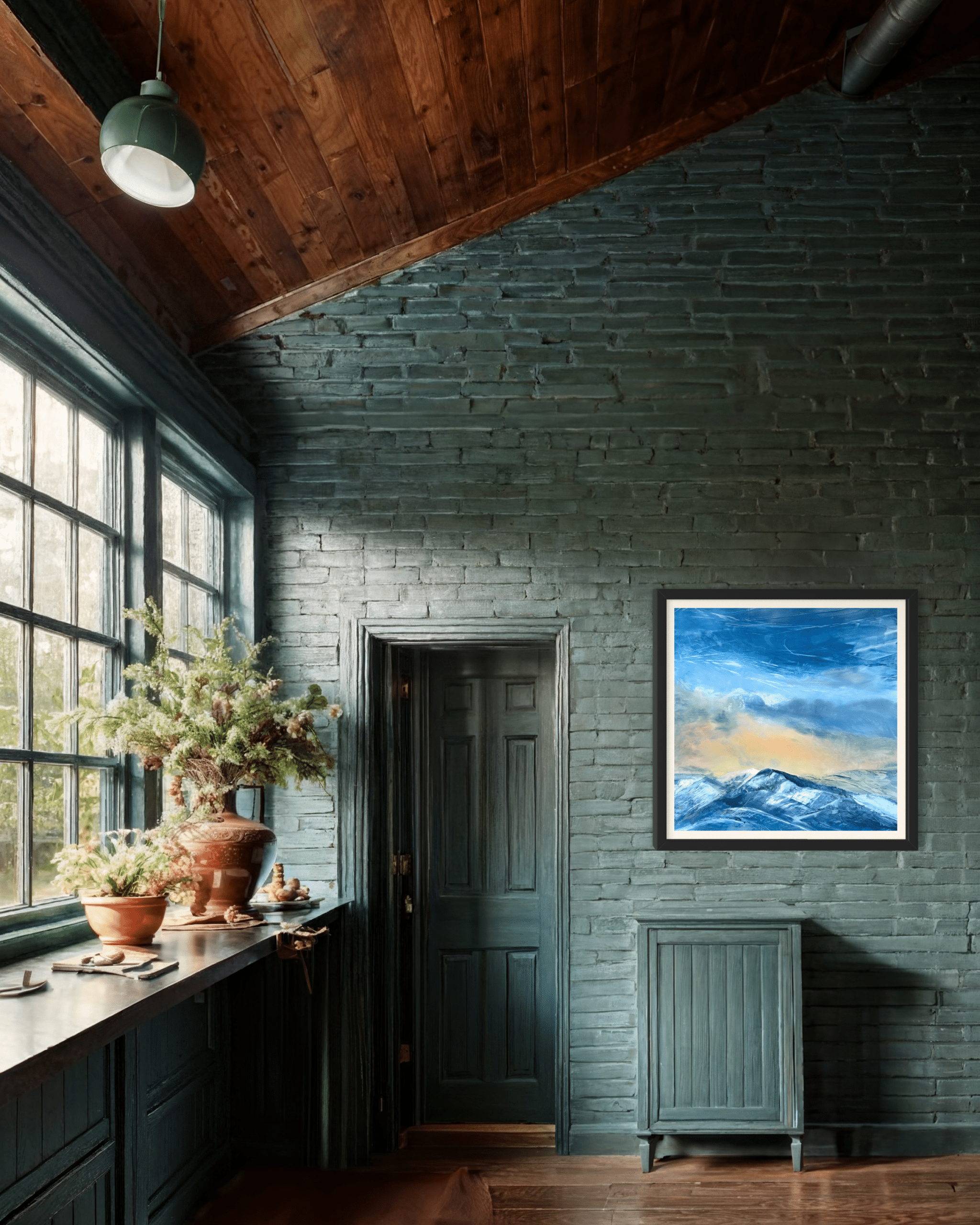 Evening Glow by Cynthia McLoughlin displayed in a rustic green-walled interior, featuring a contemporary oil painting of snow-capped Wasatch mountains at sunset with a luminous blue and gold sky, Park City, Utah.