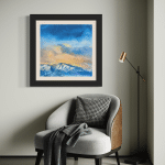 Modern mountain landscape painting "Last Run" on a pale gray wall, displayed above a stylish light gray armchair with brown leather trim in a chic corner design.